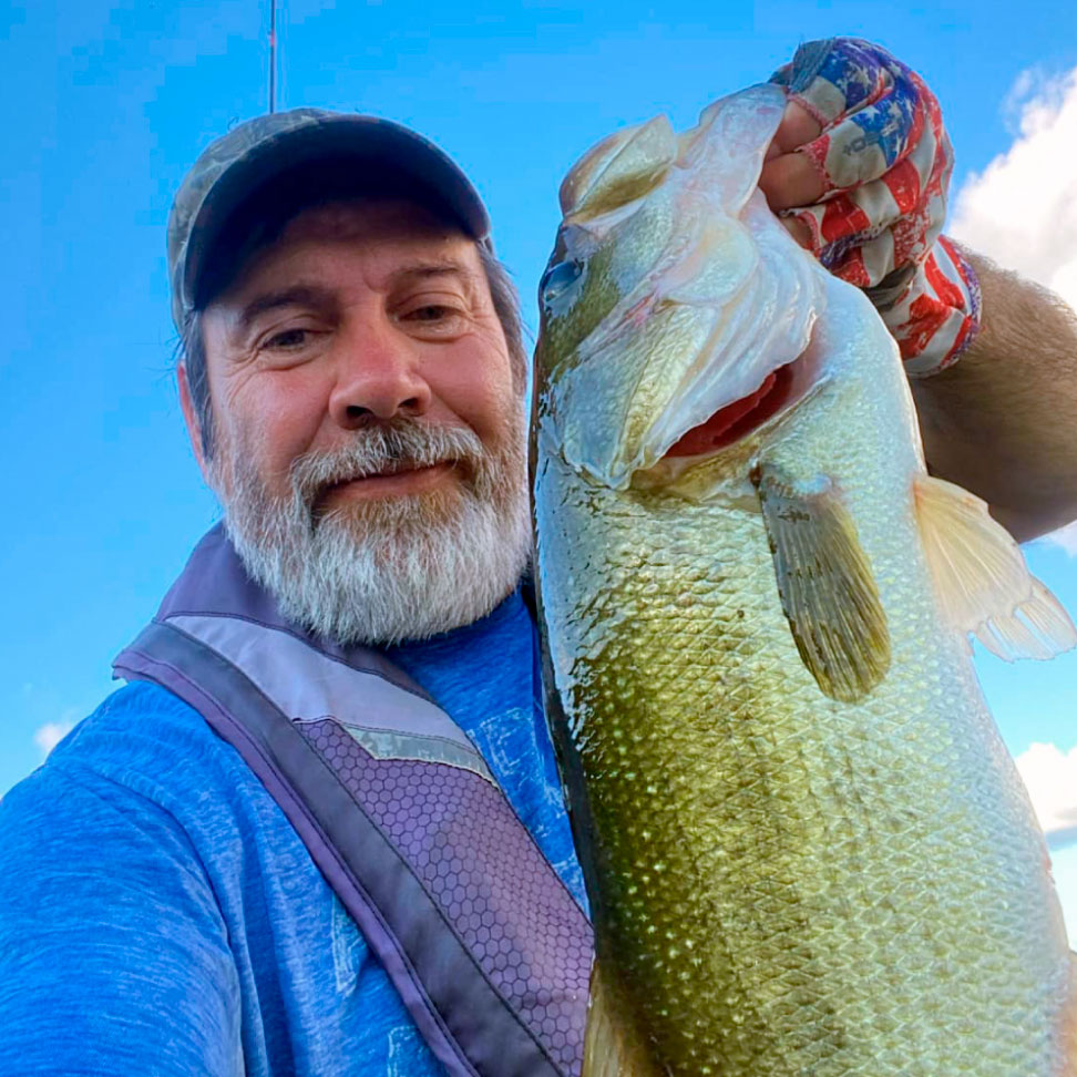 Scott-Zeleny | Minnesota Kayak Fishing Association Man with a gray beard wearing a cap and blue shirt holds a large fish up to the camera outdoors.